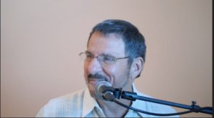 A man with glasses is speaking into a microphone.